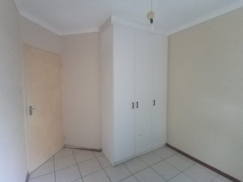 A simple, empty bedroom featuring tiled flooring and a built-in white wardrobe.