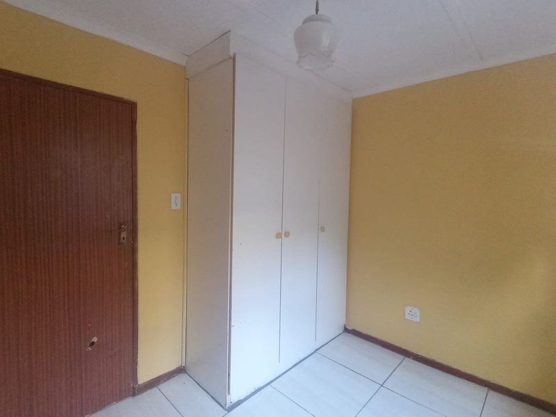 A simple bedroom featuring tiled flooring, a built-in wardrobe, and yellow painted walls, offering a blank canvas for potential updates.