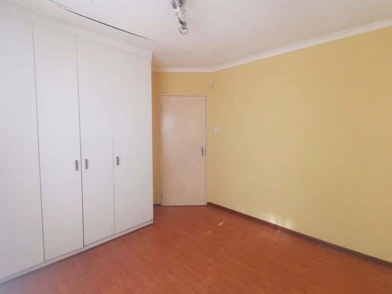 A clean, empty bedroom featuring laminate flooring, built-in cupboards, and neutral yellow walls, offering a blank canvas for personalization.