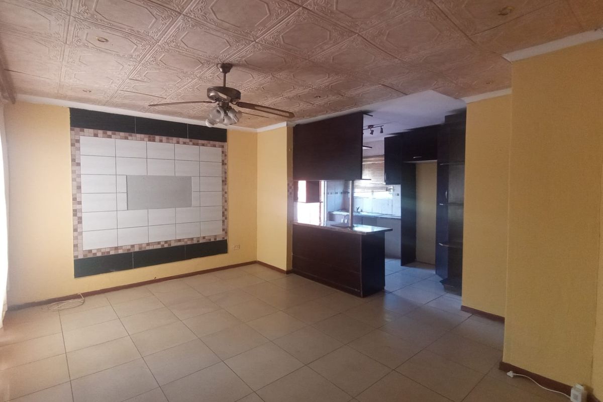 Open plan living and kitchen area featuring tiled flooring, a breakfast bar, built-in cabinetry, and a decorative ceiling with a central fan.