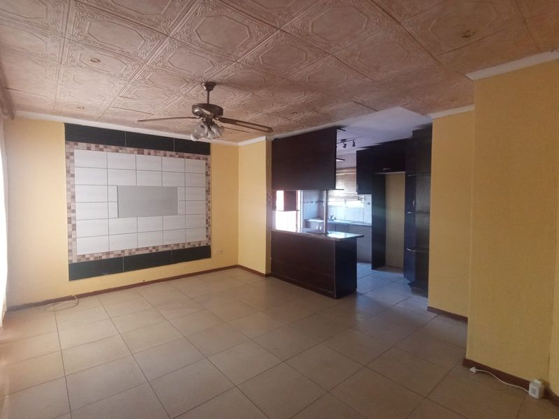 Open plan living and kitchen area featuring tiled flooring, a breakfast bar, built-in cabinetry, and a decorative ceiling with a central fan.