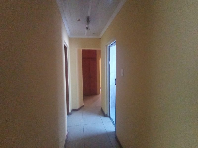 A narrow residential hallway featuring tiled flooring and access to adjacent rooms, including a built-in storage cupboard.