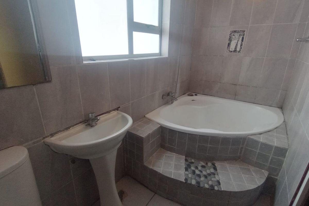 A dated bathroom featuring a pedestal basin, a built-in corner bathtub with tiled surround, and neutral wall tiling throughout.