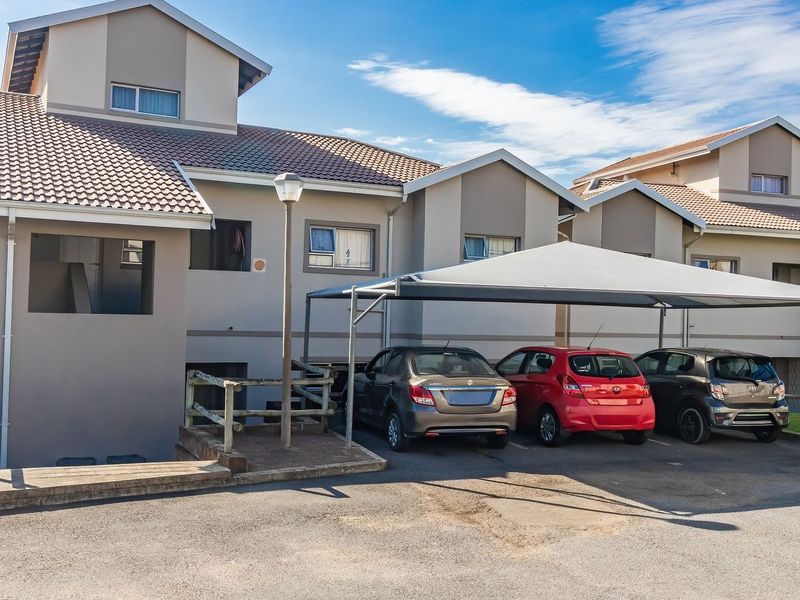 Front elevation of a townhouse complex featuring a covered carport, paved driveway, and multi-level architectural design with tiled roofing.