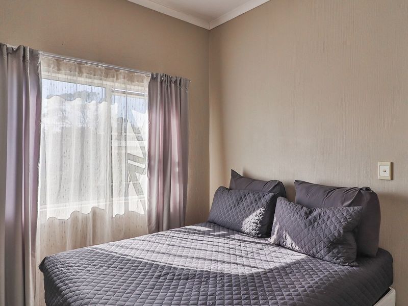 A bedroom featuring a sliding window with curtains and neutral wall finishes, providing a functional and comfortable sleeping space.