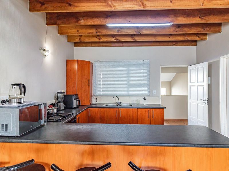 Functional kitchen featuring exposed timber ceiling beams, laminate cabinetry, dark countertops, and a breakfast bar, offering a practical layout for daily use.