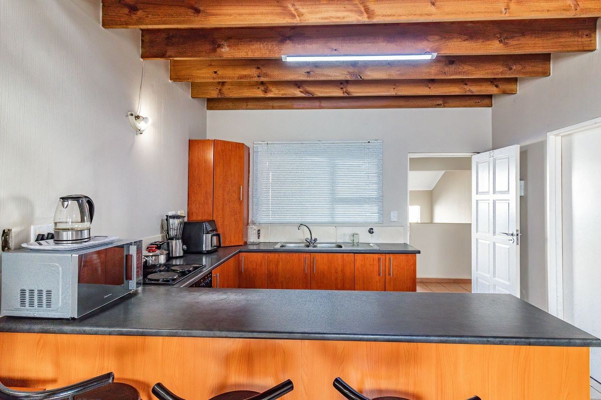 Functional kitchen featuring exposed timber ceiling beams, laminate cabinetry, dark countertops, and a breakfast bar, offering a practical layout for daily use.