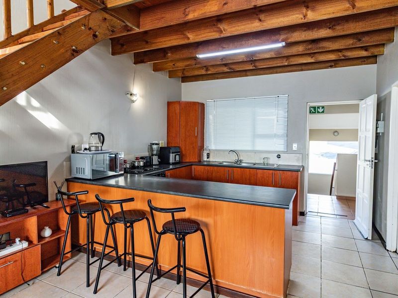 Open-plan kitchen featuring timber cabinetry, laminate countertops, and exposed wooden ceiling beams, with an adjacent staircase leading to the upper level.