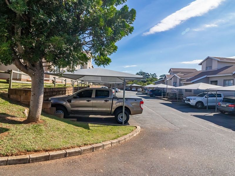 Exterior view of the townhouse complex driveway featuring paved parking areas with shade cloth carports and landscaped retaining walls.