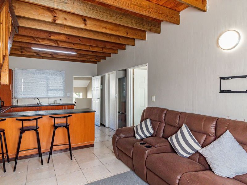 Open-plan living area featuring exposed timber ceiling beams, a tiled floor, and a functional kitchen with a breakfast bar and timber cabinetry.
