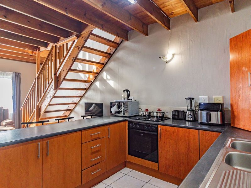 Open plan kitchen featuring timber cabinetry, built-in oven and hob, and a wooden staircase leading to the upper level with exposed ceiling beams.