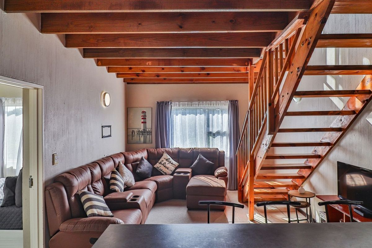A cozy living room featuring exposed timber ceiling beams and a wooden staircase, creating a warm and rustic atmosphere.