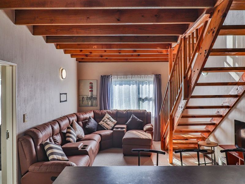 A cozy living room featuring exposed timber ceiling beams and a wooden staircase, creating a warm and rustic atmosphere.