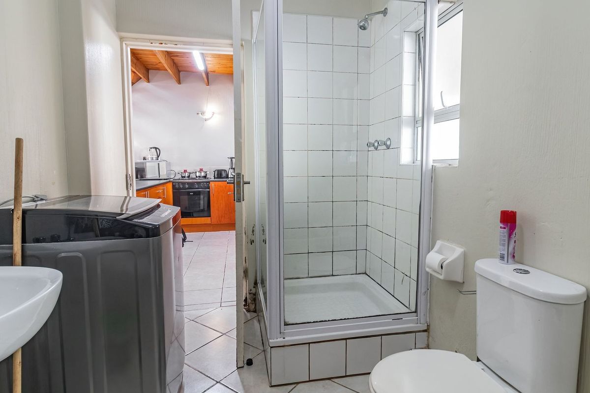 A functional bathroom featuring a shower enclosure, toilet, and pedestal basin, with tiled flooring and direct access to the adjacent kitchen area.