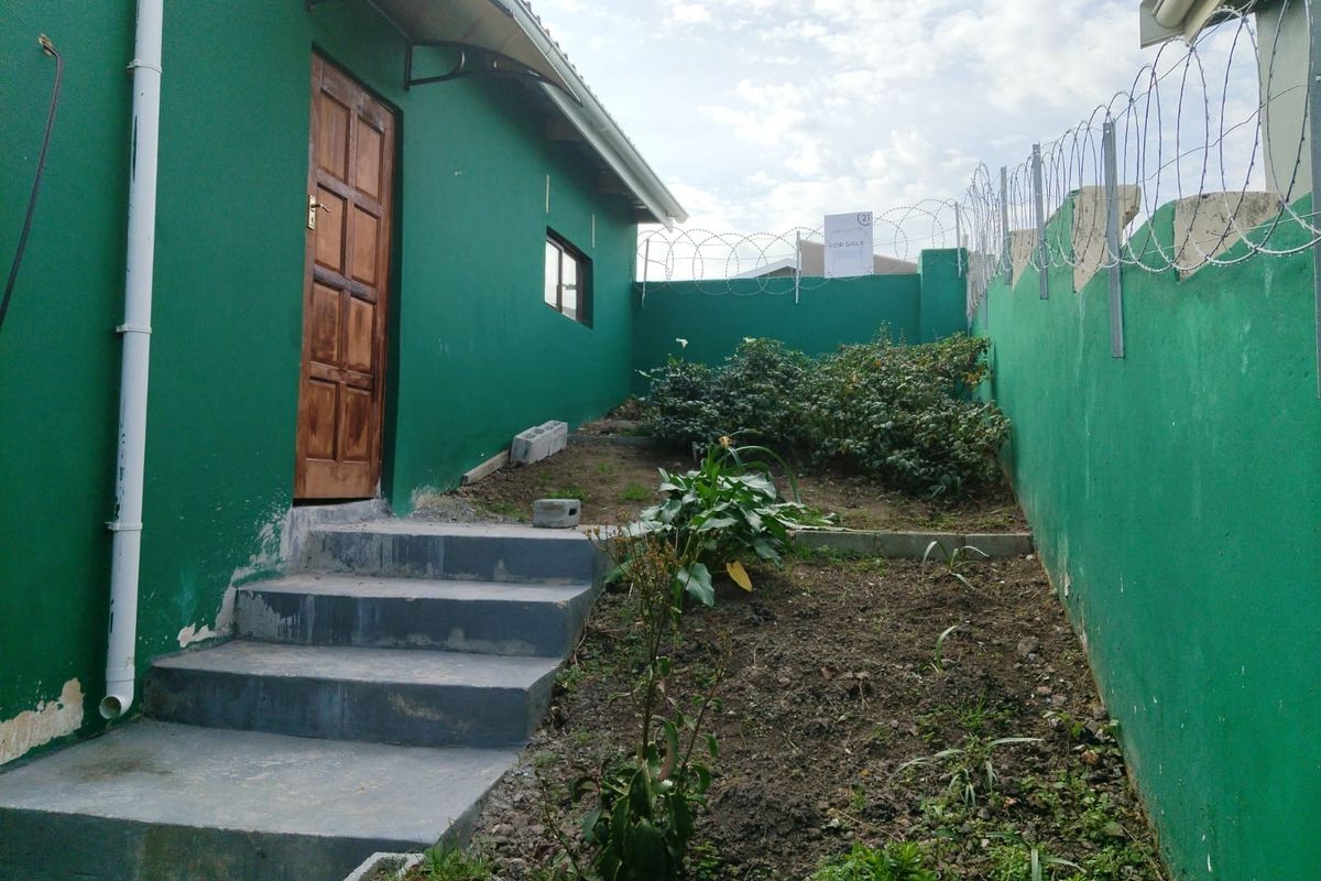 Rear exterior view of the property featuring a green painted wall, concrete steps, and a perimeter wall secured with razor wire.