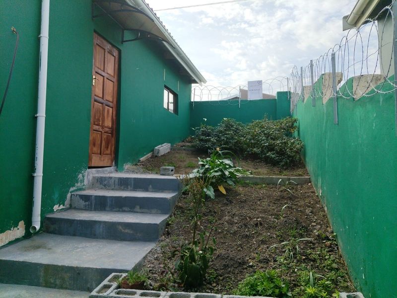 Rear exterior view of the property featuring a green painted wall, concrete steps, and a perimeter wall secured with razor wire.
