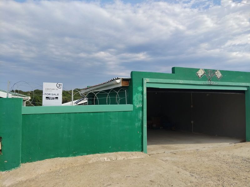 A detached garage structure with a concrete driveway, perimeter walling, and security razor wire, featuring an open-front design.