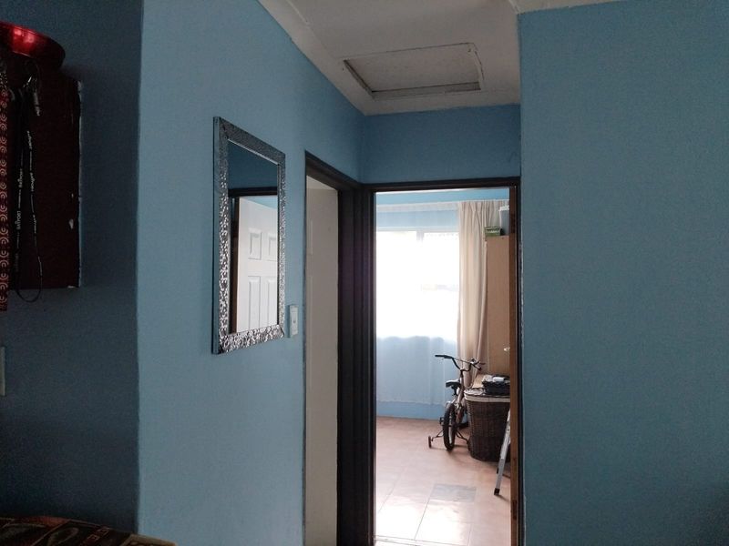 A functional hallway space connecting rooms, featuring a ceiling access hatch and neutral blue wall paint.