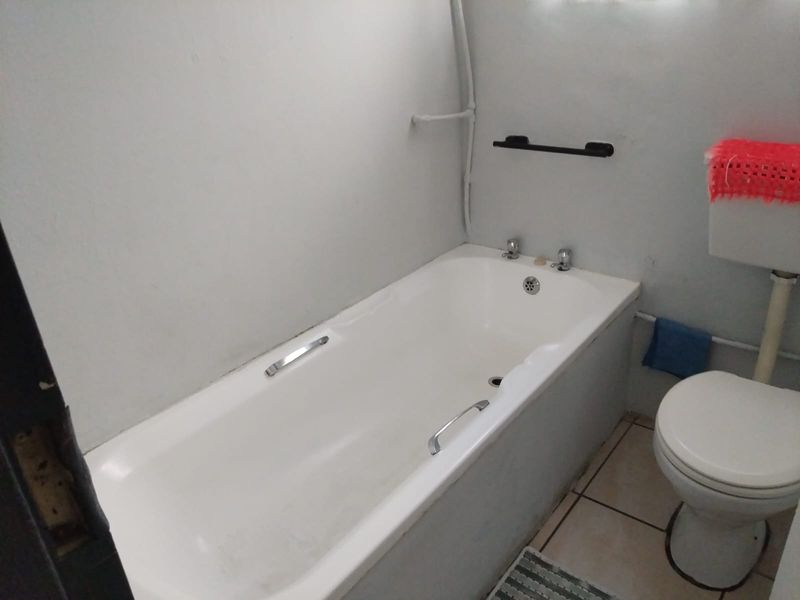 A functional bathroom featuring a standard bathtub, toilet, and tiled flooring, requiring cosmetic updates to improve its overall condition and aesthetic appeal.