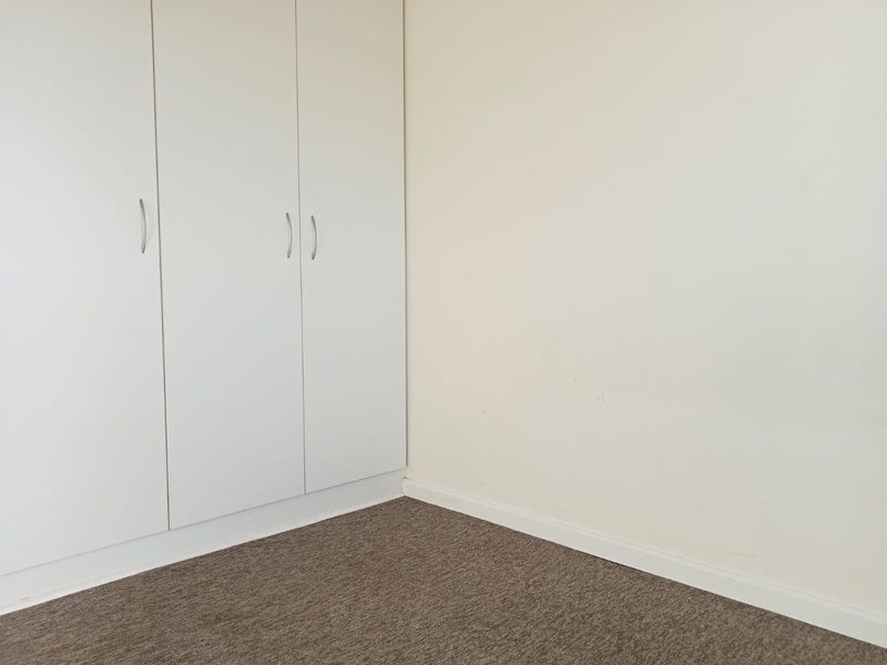 A clean, empty bedroom corner featuring neutral carpet flooring and white built-in wardrobes with modern handles.