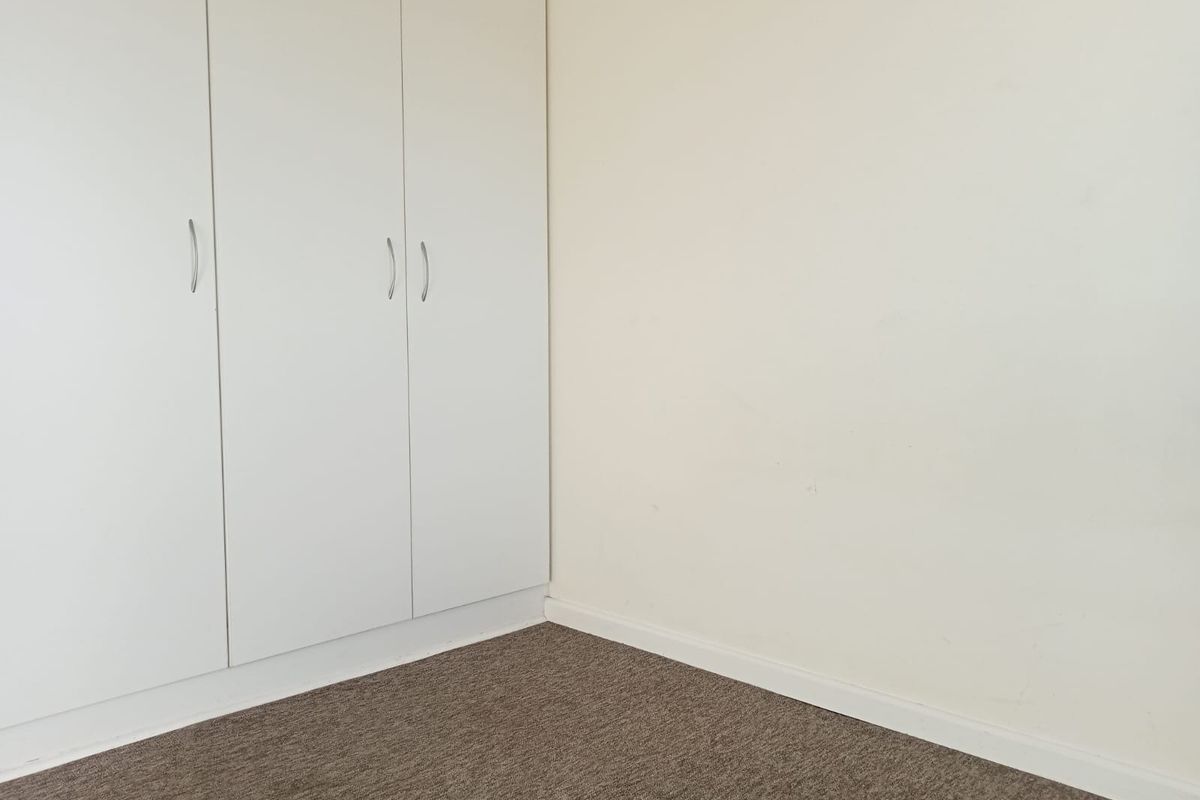 A clean, empty bedroom corner featuring neutral carpet flooring and white built-in wardrobes with modern handles.