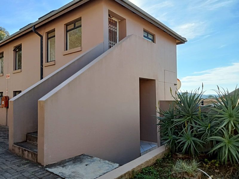 Exterior view of an apartment building featuring a concrete staircase, security gate, and paved walkway access.