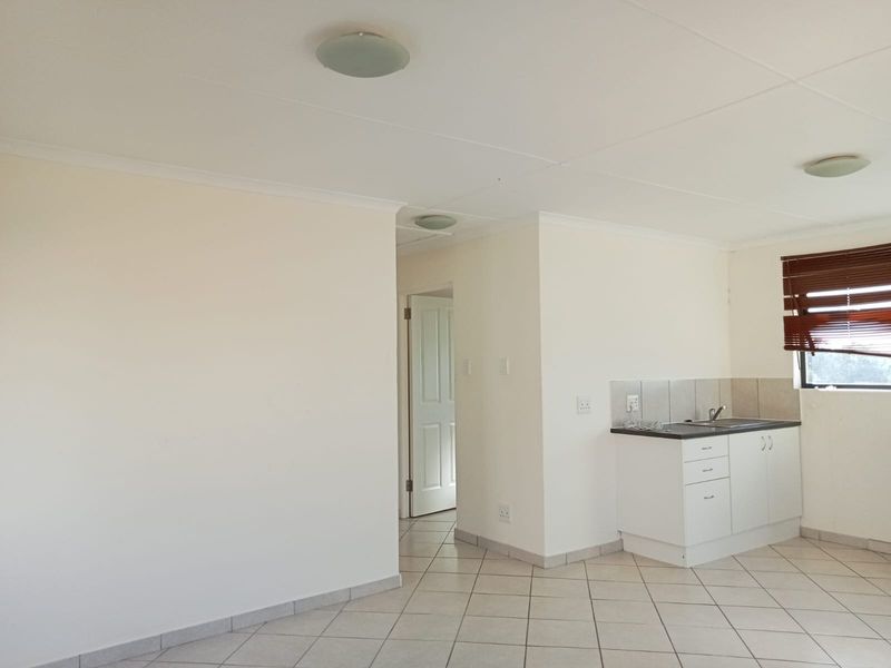 An open-plan living and kitchen area featuring tiled flooring, neutral walls, and compact kitchen cabinetry with a sink.