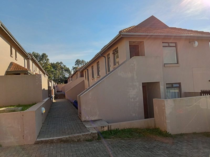 Exterior view of a multi-unit apartment complex featuring paved walkways, tiled roofing, and external wall lighting.