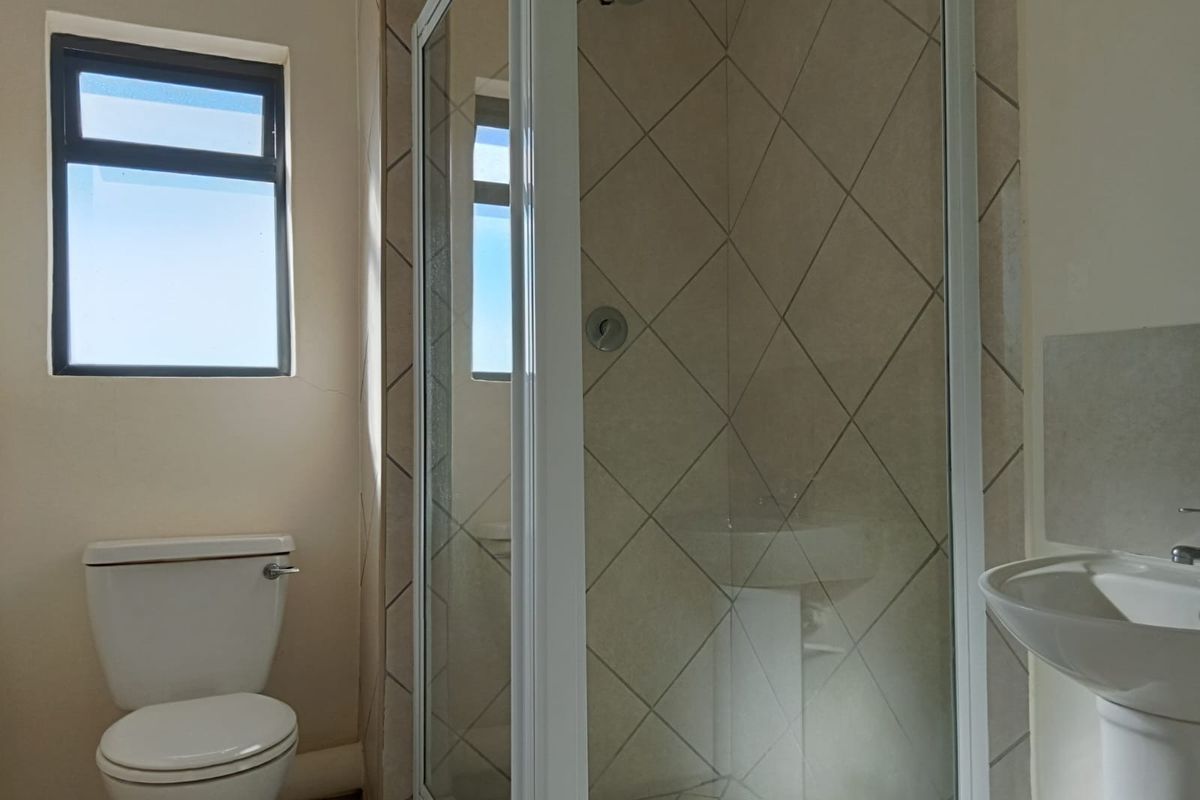 A functional bathroom featuring a shower enclosure, pedestal basin, and toilet, with diamond-patterned wall tiling and a window for natural light.