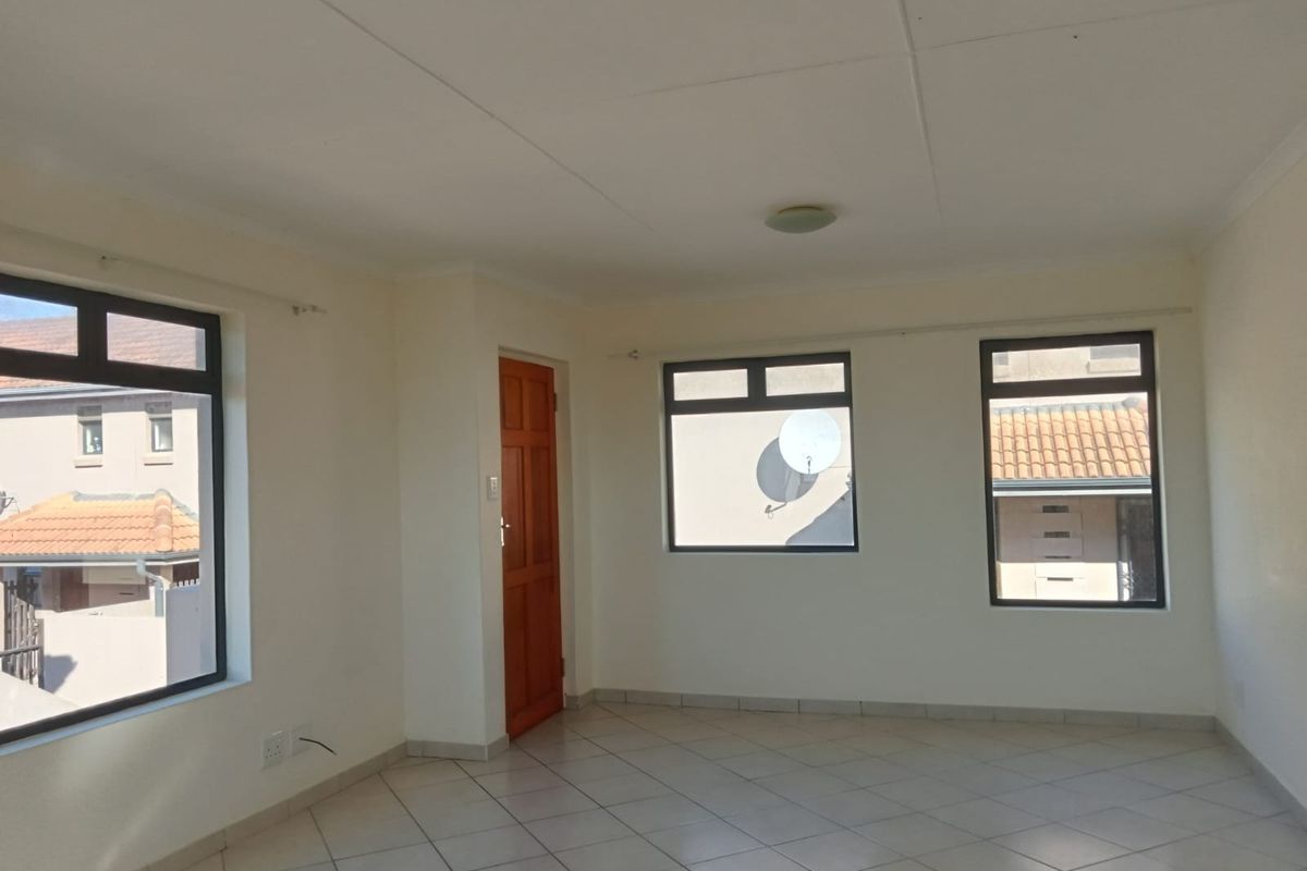A bright, empty living area featuring neutral tiled flooring, large aluminium-framed windows, and clean white walls, ready for personalization.