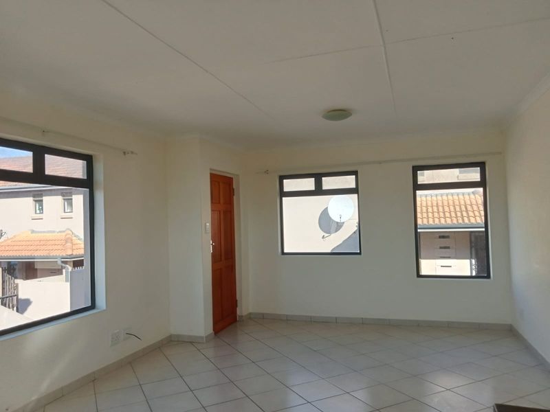 A bright, empty living area featuring neutral tiled flooring, large aluminium-framed windows, and clean white walls, ready for personalization.