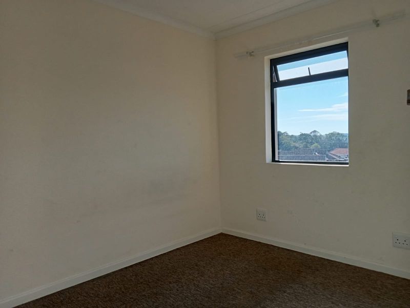 An empty bedroom featuring carpet flooring, neutral walls, and a window with a view, providing a blank canvas for personalization.