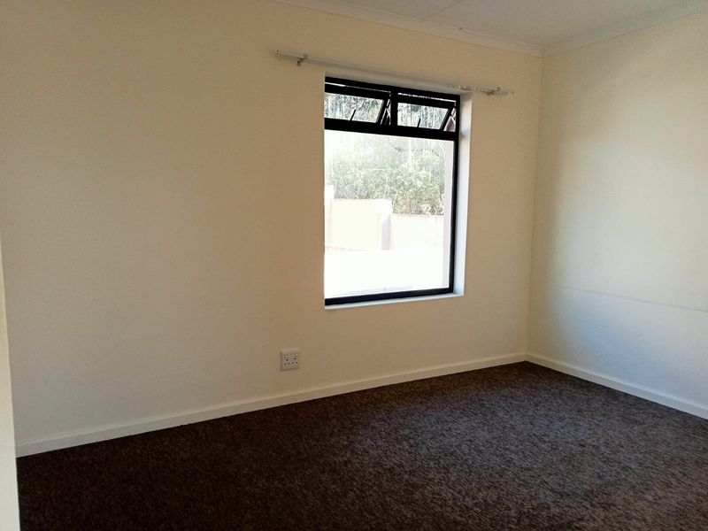 A clean, empty bedroom featuring neutral walls, carpeted flooring, and a window with a curtain rod installed.