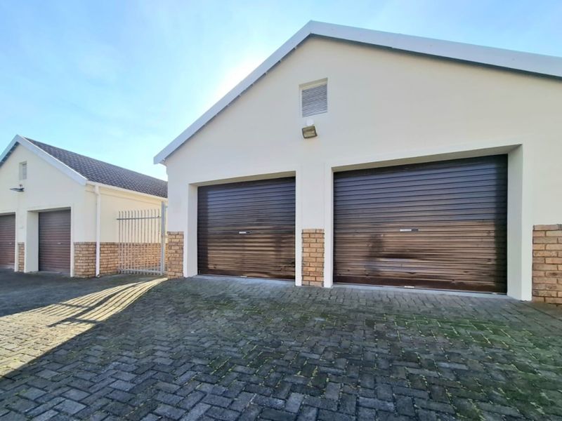 Exterior view of a townhouse complex featuring a double garage and an adjacent single garage with paved driveway access.