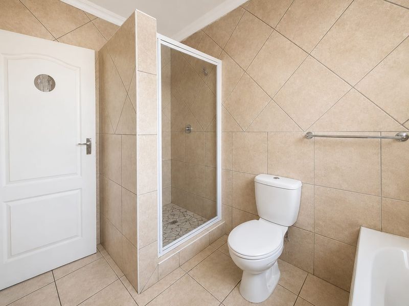 A functional bathroom featuring a shower enclosure, toilet, and bathtub with neutral wall and floor tiling.
