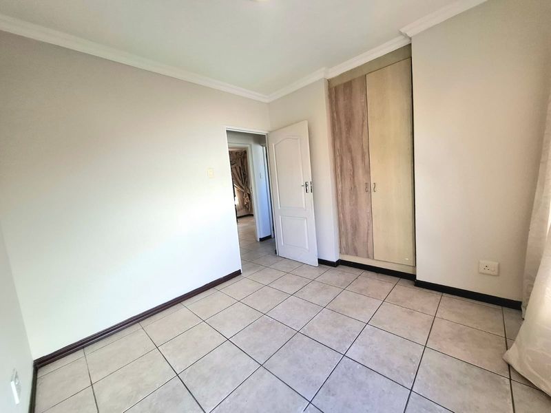 A clean, empty bedroom featuring neutral tiled flooring, built-in cupboards with wood-finish doors, and classic coving detail.