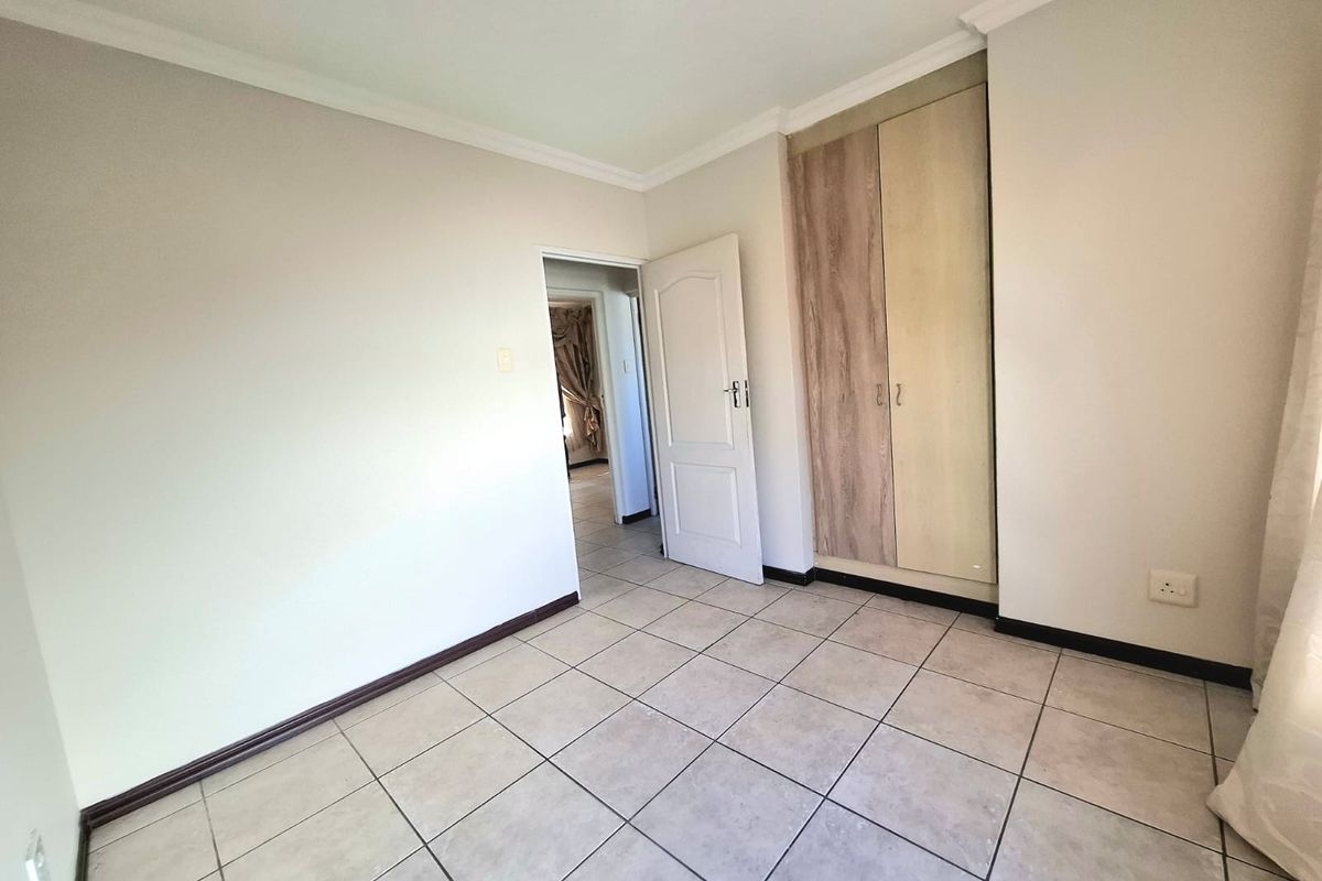 A clean, empty bedroom featuring neutral tiled flooring, built-in cupboards with wood-finish doors, and classic coving detail.