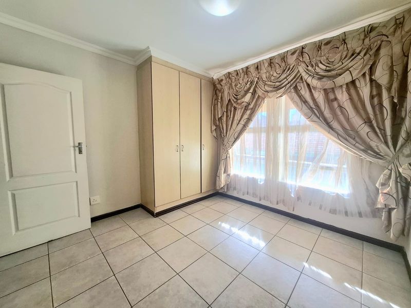 A bright, empty bedroom featuring neutral tiled flooring, built-in cupboards, and coved ceiling detailing, offering a clean canvas for personalization.