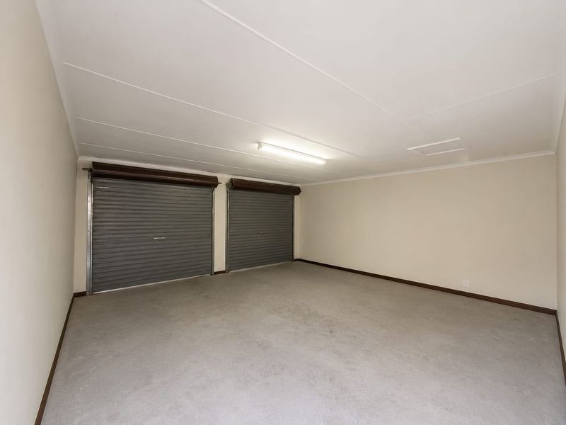 A spacious, clean, and empty double garage featuring dual roller doors, concrete flooring, and functional overhead lighting.
