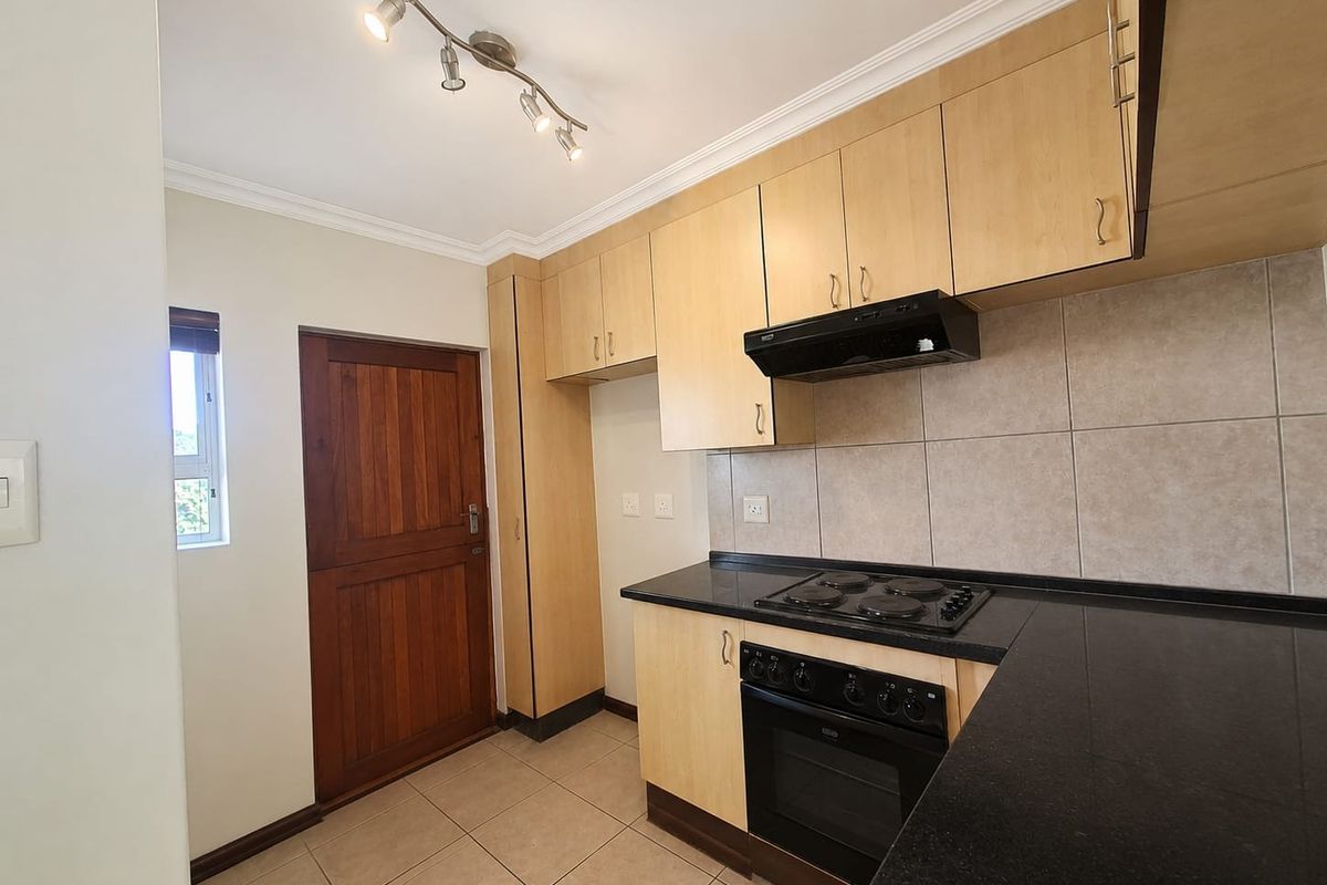 A functional kitchen featuring light wood cabinetry, black granite countertops, built-in oven and hob, and tiled flooring.