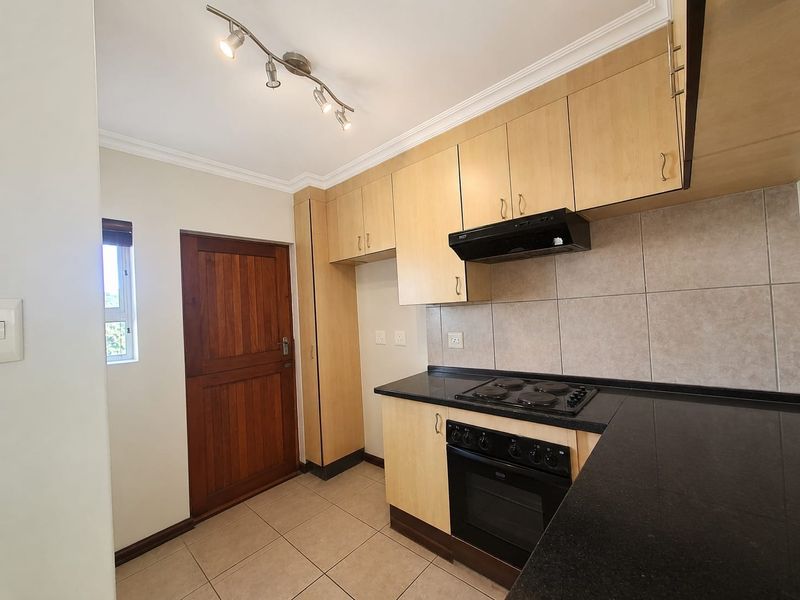 A functional kitchen featuring light wood cabinetry, black granite countertops, built-in oven and hob, and tiled flooring.