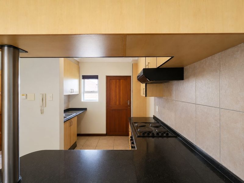 A functional kitchen featuring light wood cabinetry, black granite countertops, an integrated electric hob with extractor fan, and tiled backsplash.