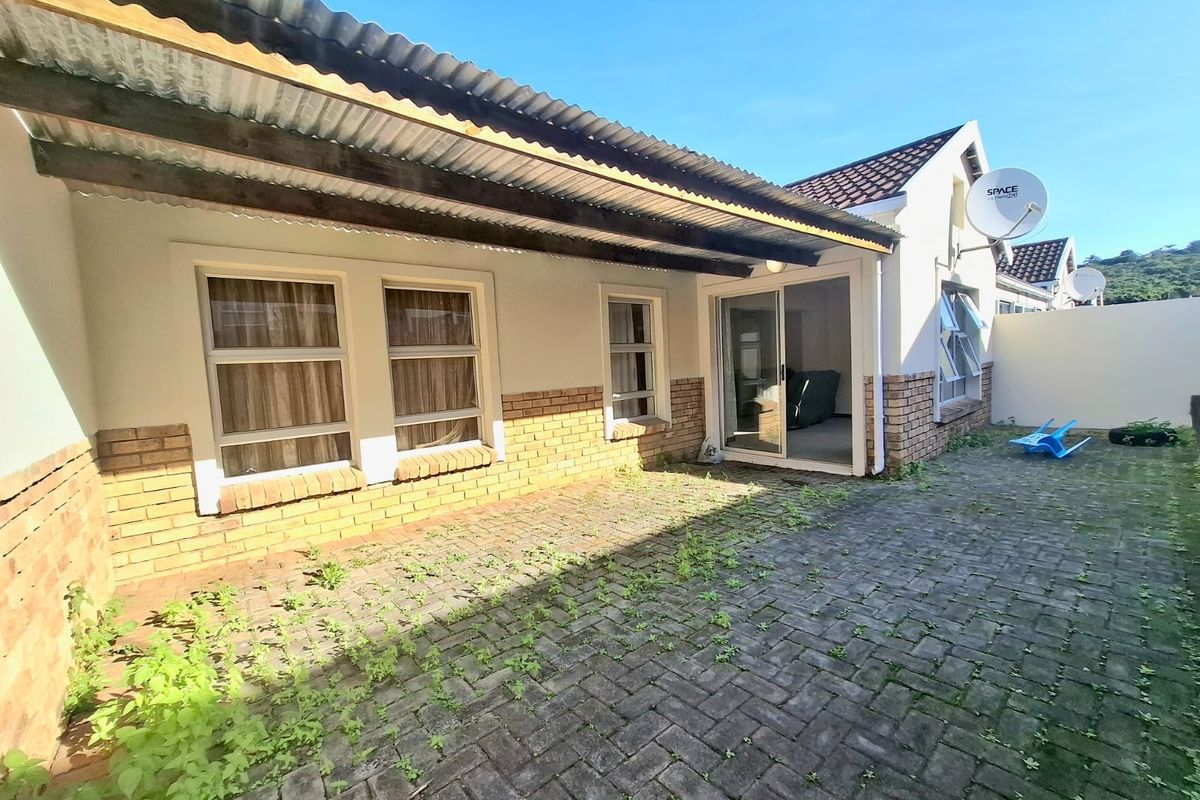 Rear exterior view of the townhouse featuring a paved patio area, sliding glass door access, and a corrugated metal roof covering.