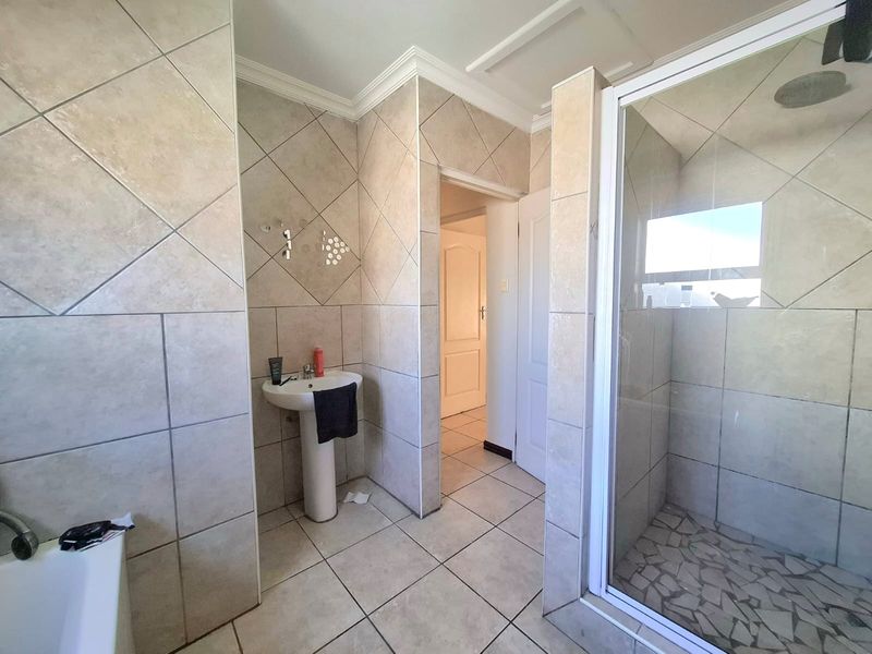 A functional bathroom featuring a pedestal sink, a glass-enclosed shower with a rain shower head, and neutral floor-to-ceiling tiling.