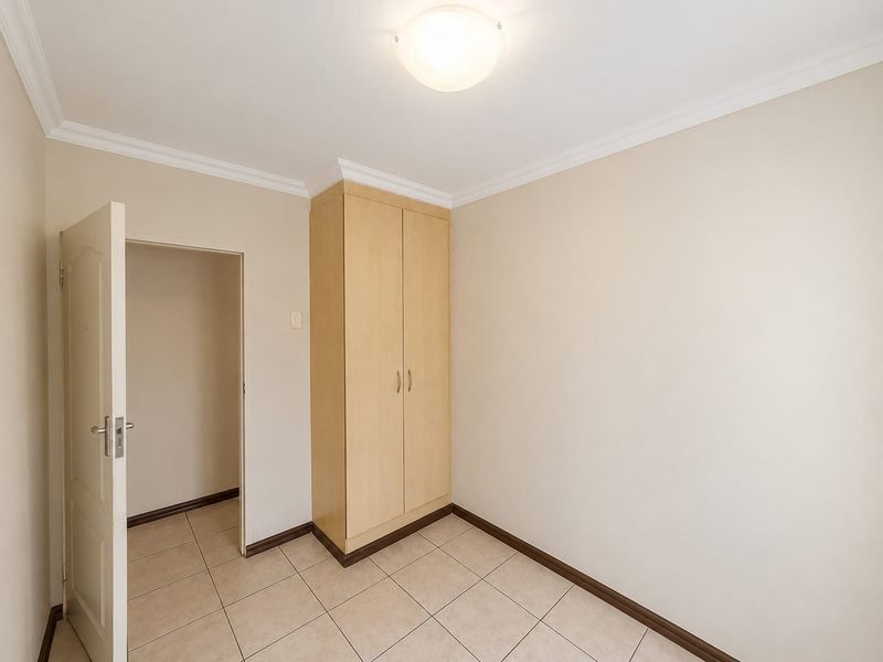 A clean, empty bedroom featuring neutral tiled flooring, a built-in wooden wardrobe, and coved ceiling detailing.