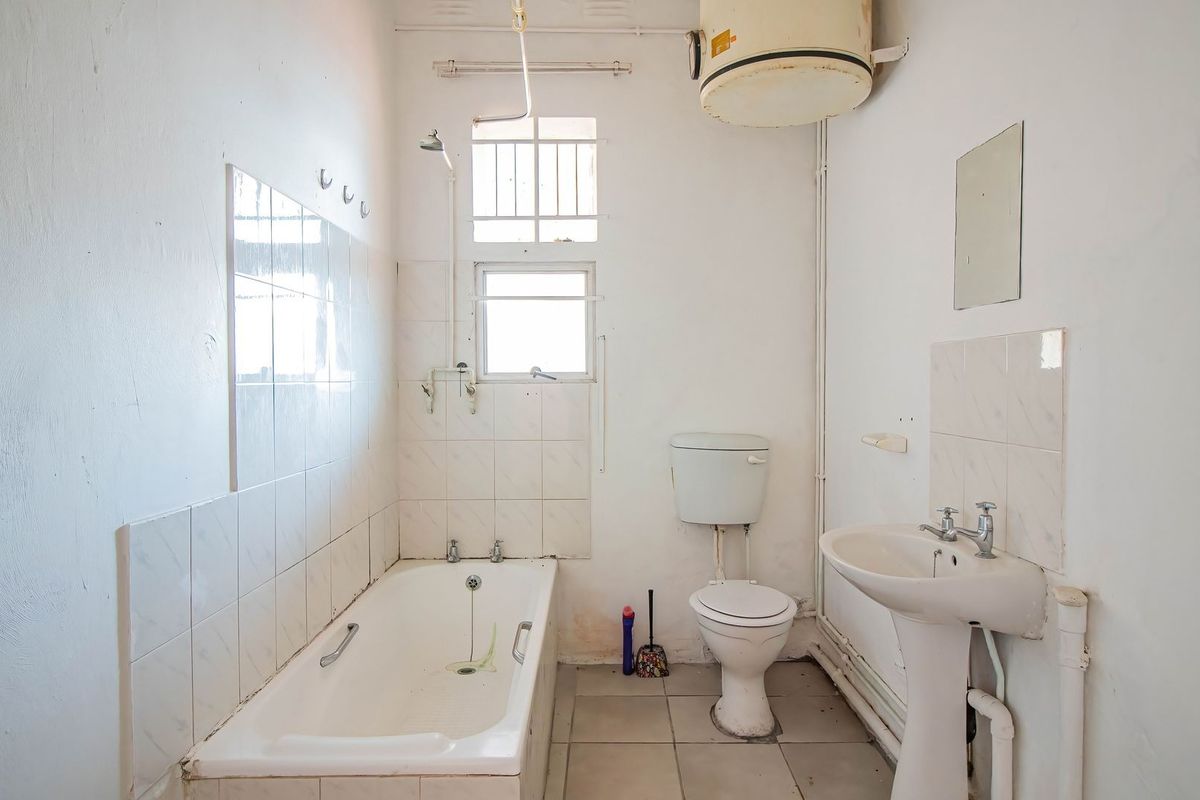 A dated bathroom featuring a standard bathtub, pedestal basin, and toilet, with exposed plumbing and wall-mounted geyser, requiring modernization and cosmetic updates.