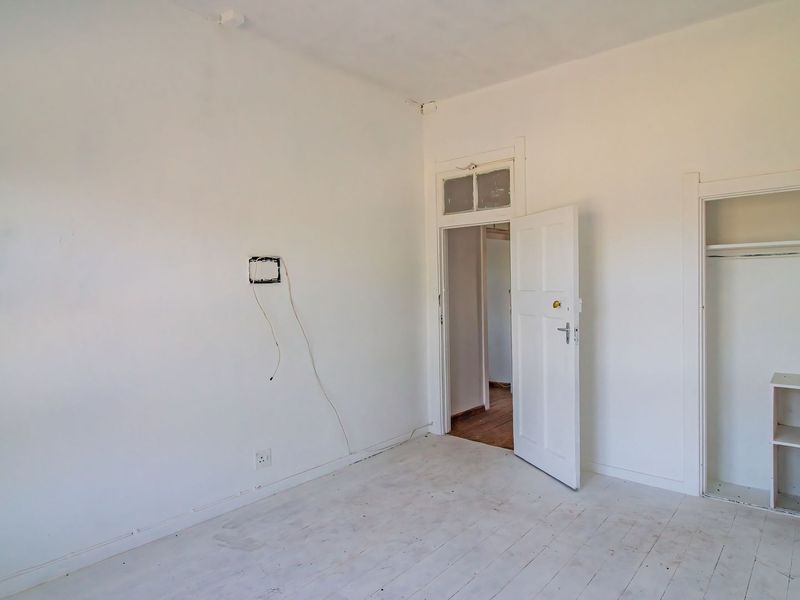 An empty bedroom featuring white painted wooden floors, a built-in closet, and a transom window above the doorway.