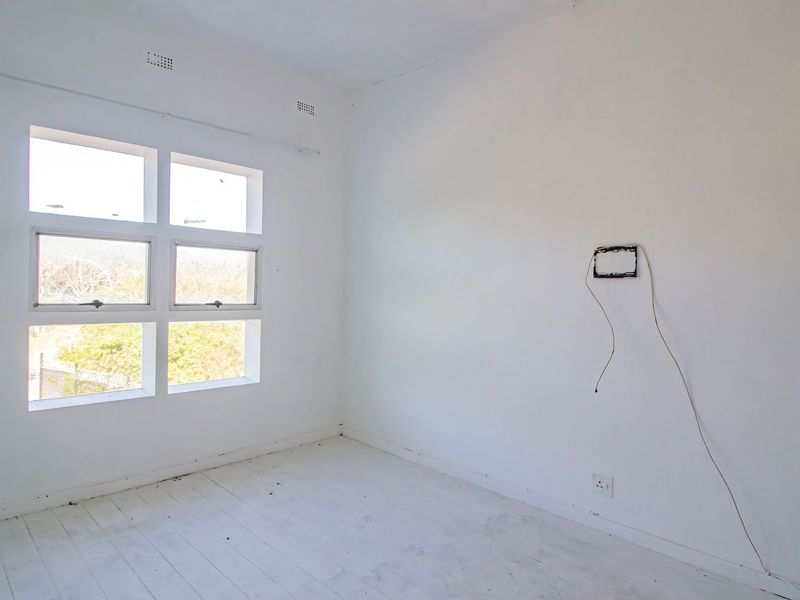 An empty bedroom featuring white painted timber floors, a multi-pane window, and exposed electrical wiring on the wall.