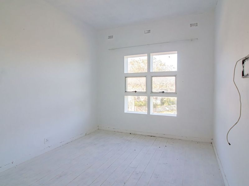 An empty bedroom featuring painted timber flooring, a multi-pane window, and exposed electrical wiring, offering a blank canvas for renovation.