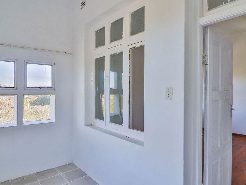 A vacant hallway area featuring a mix of tiled and timber flooring, with multiple windows and a classic panel door leading to an adjacent room.